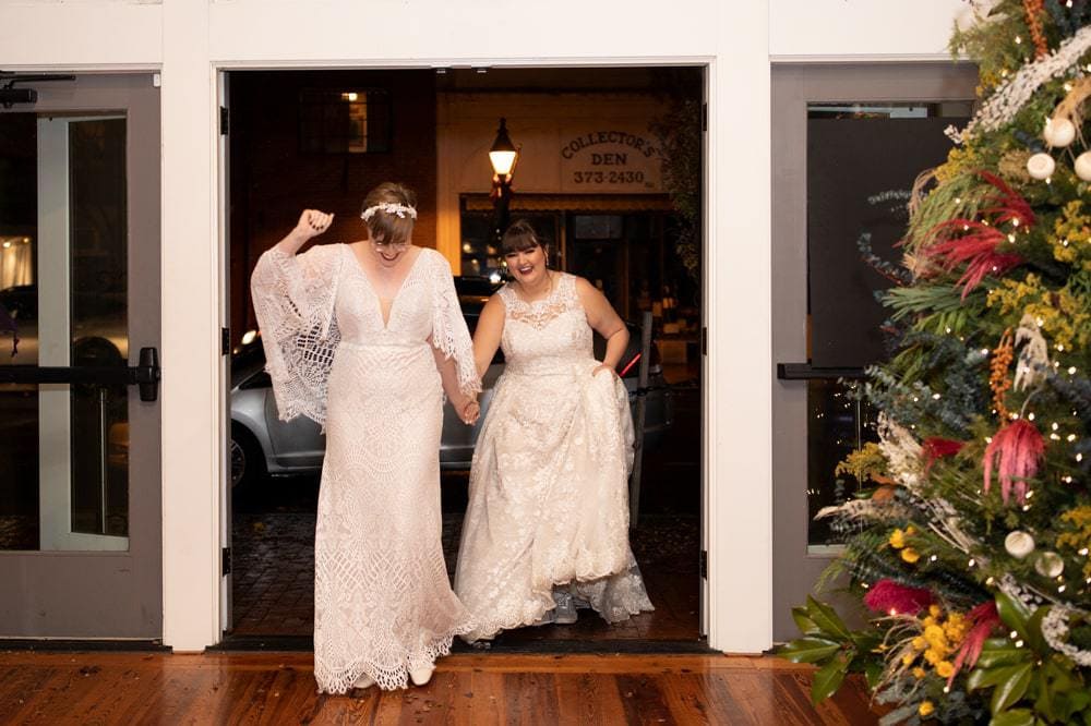 Two brides cheer and laugh as they enter their reception at an urban venue in Fredericksburg, Virginia
