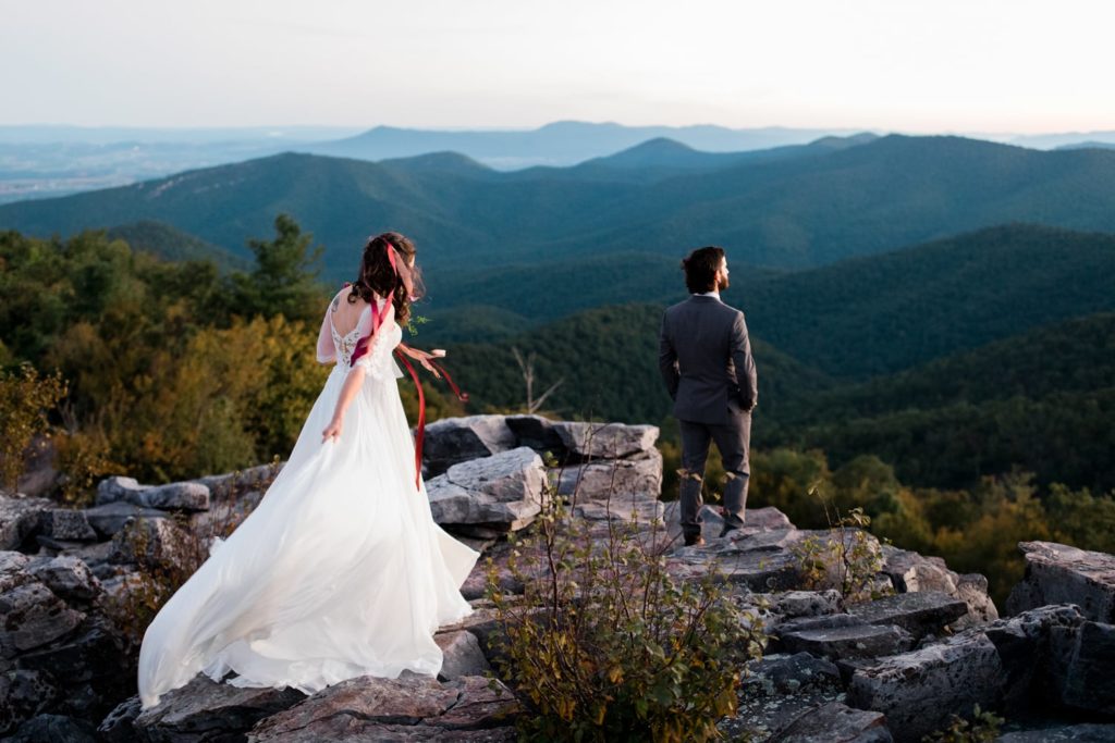 A bride approaches her groom on top of a mountain. They are about to do a first look at a spot in Shenandoah National Park before their micro wedding ceremony