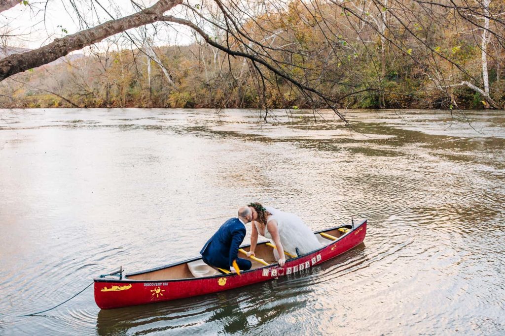 A bride and groom kiss in a red canoe decorated with a "we eloped" sign