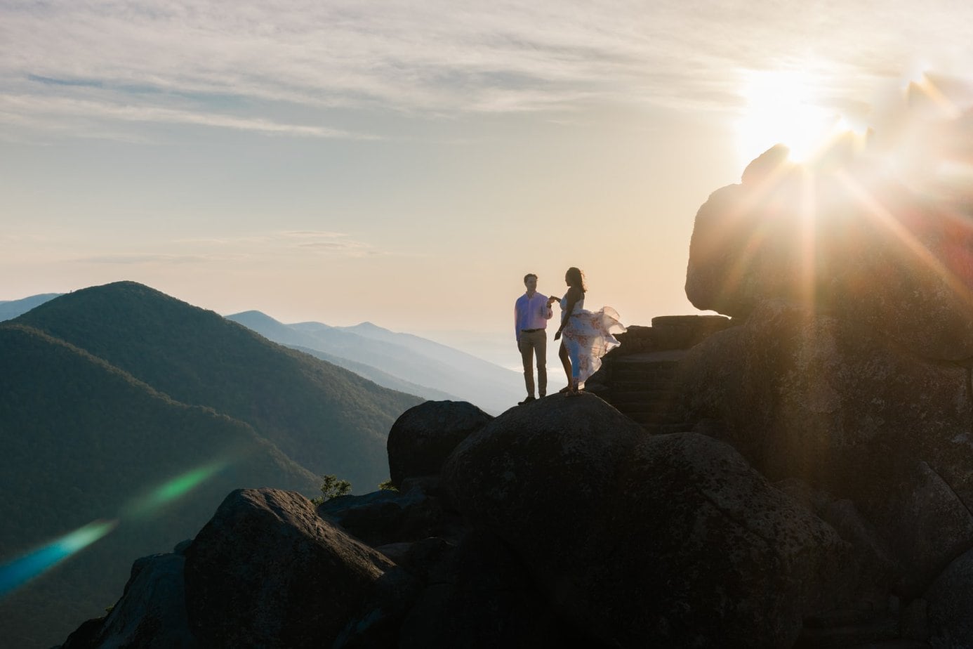 A man and woman stand silhouetted on a dramatic mountain landscape