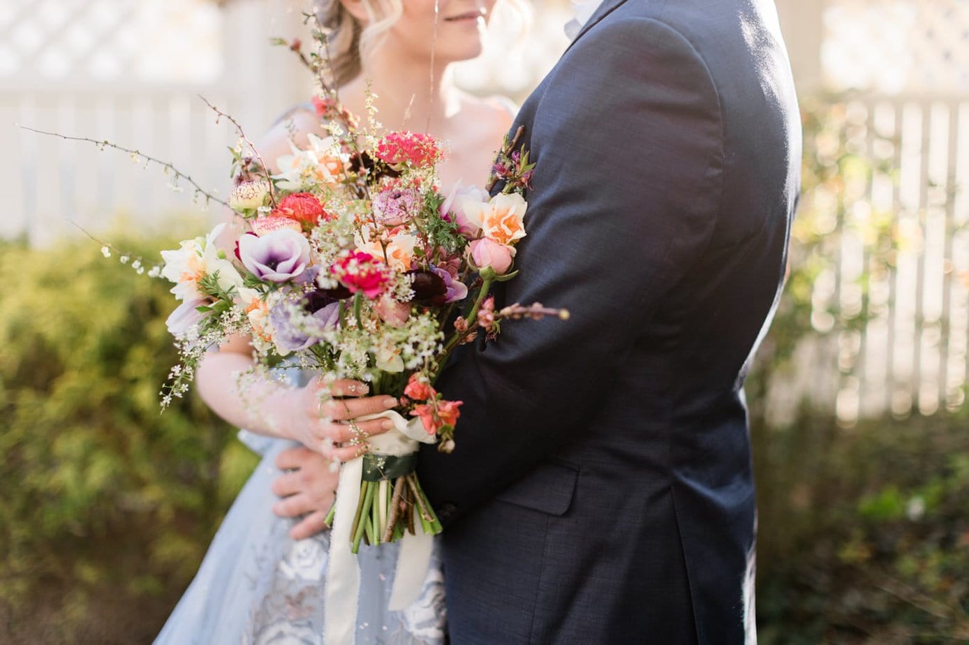 A couple look at each other during a romantic garden wedding editorial shoot in downtown Roanoke. The bride is wearing a blue dress and is holding a colorful boho bouquet