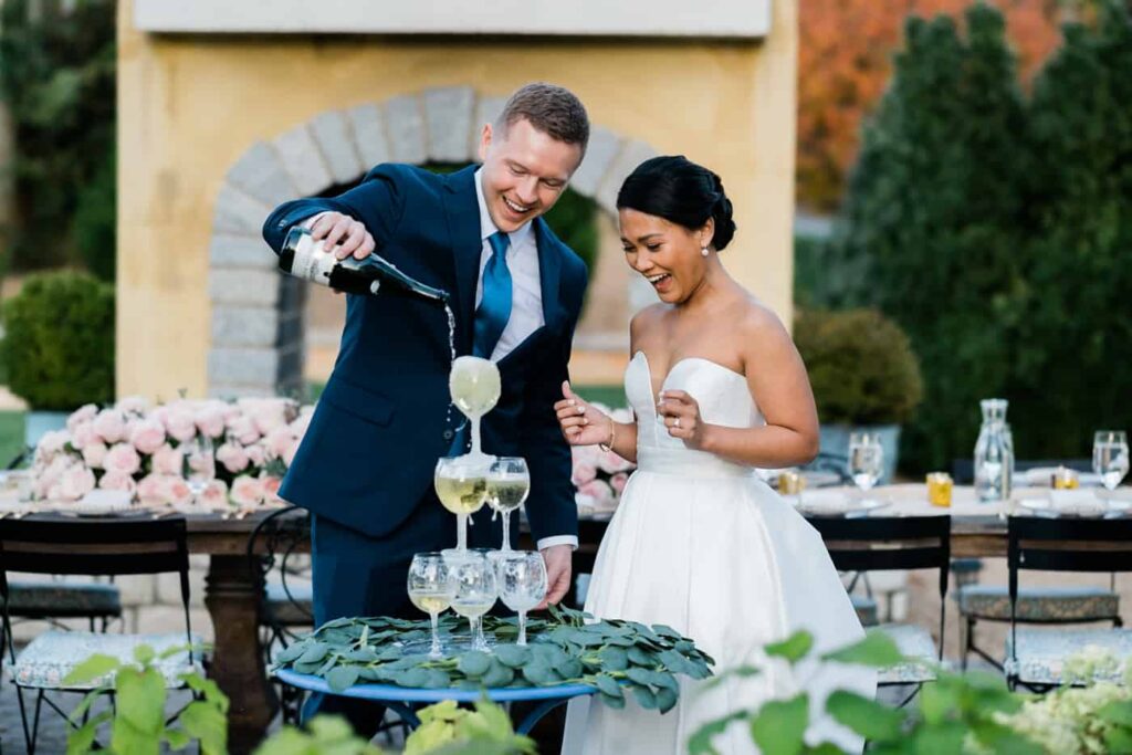 A couple pours a champagne tour during their luxury micro wedding in Charlottesville. He is holding the champagne, she is laughing