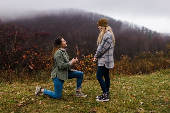 A woman gets down on one knee to propose to her girlfriend during a surprise proposal in Shenandoah National Park