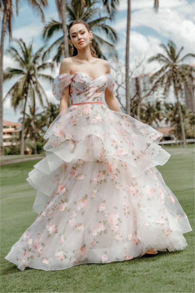 A woman wears a floral printed organza gown with tiers. 