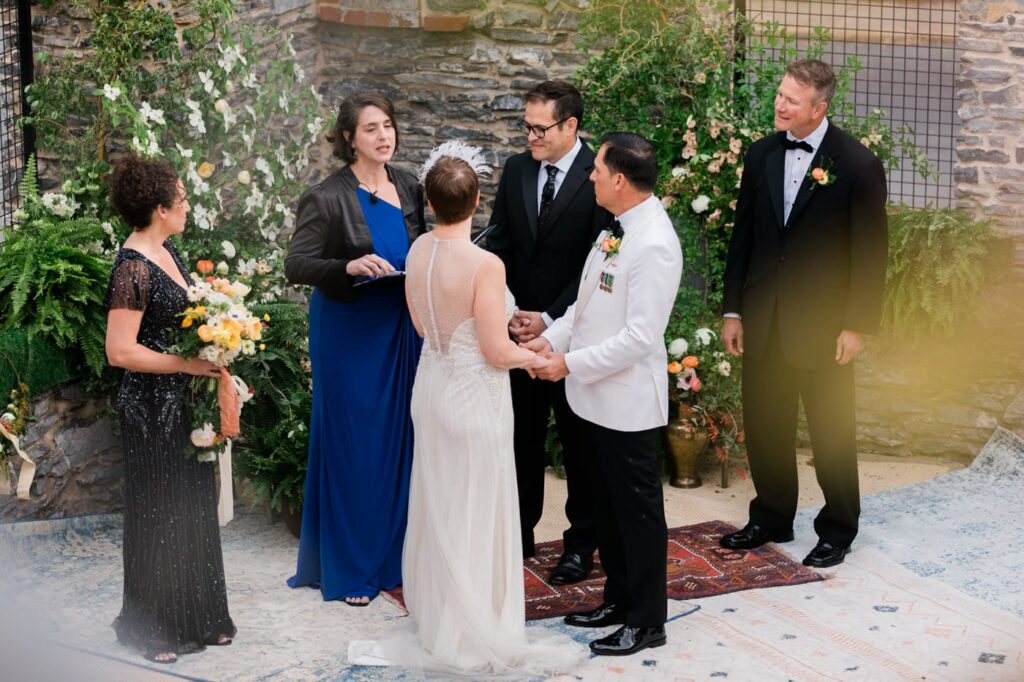 A couple stands at the altar surrounded by two officiants and their friends during their wedding ceremony