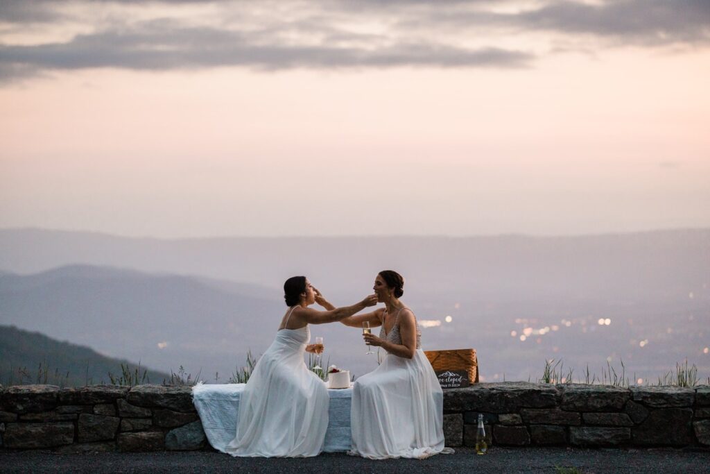 A lesbian couple celebrates their elopement in Shenandoah National Park by cutting a cake and feeding it to one another. 