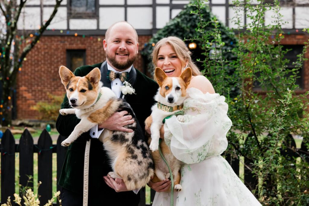 A couple stands with their two dogs in their wedding attire. 